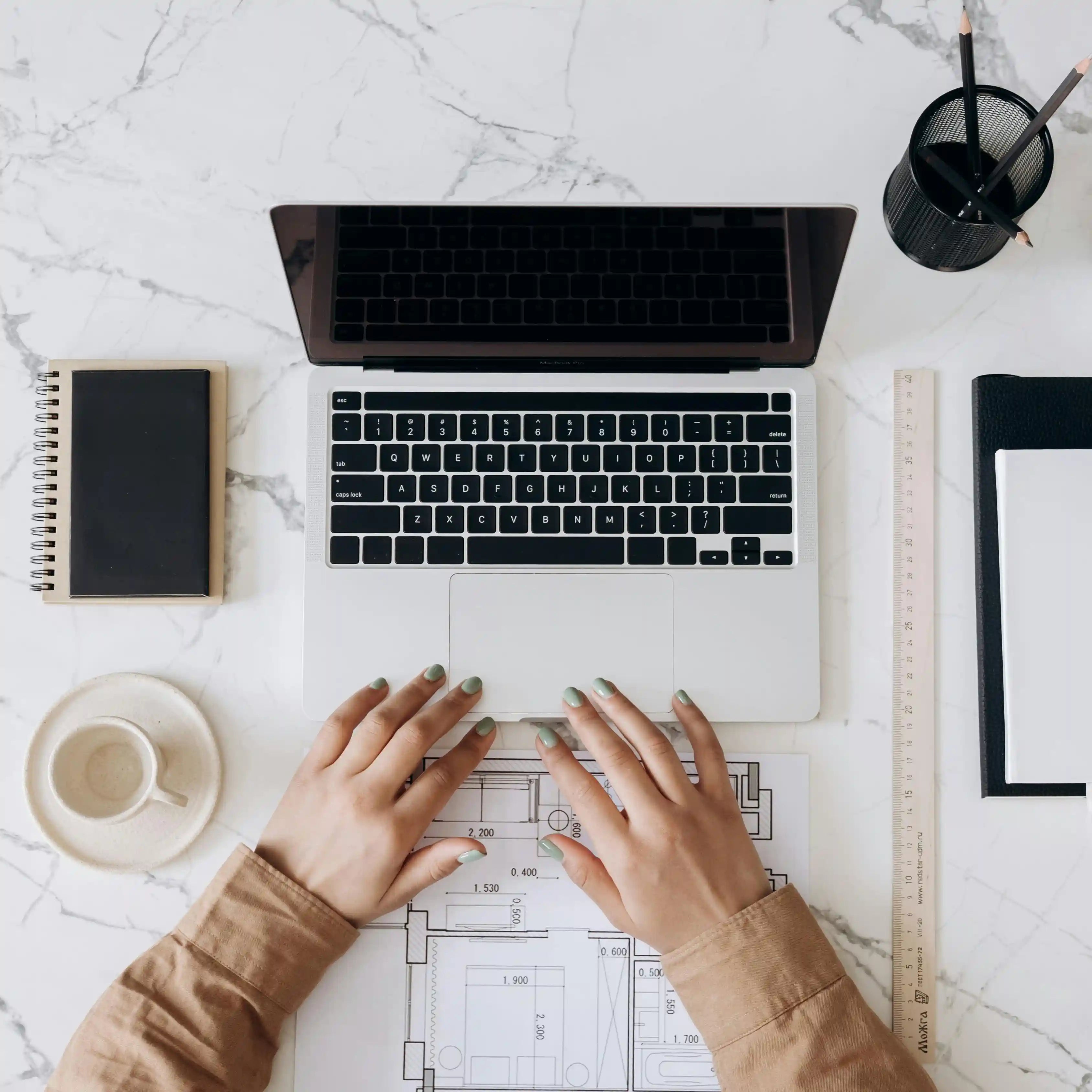 Overhead view of a woman working on a laptop with notebooks and coffee on a marble desk, reflecting focus and gut balance